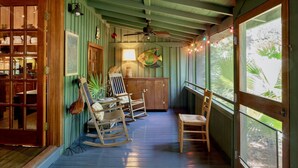 Een houten veranda met schommelstoelen, een plafondventilator en uitzicht op groen door grote ramen.
