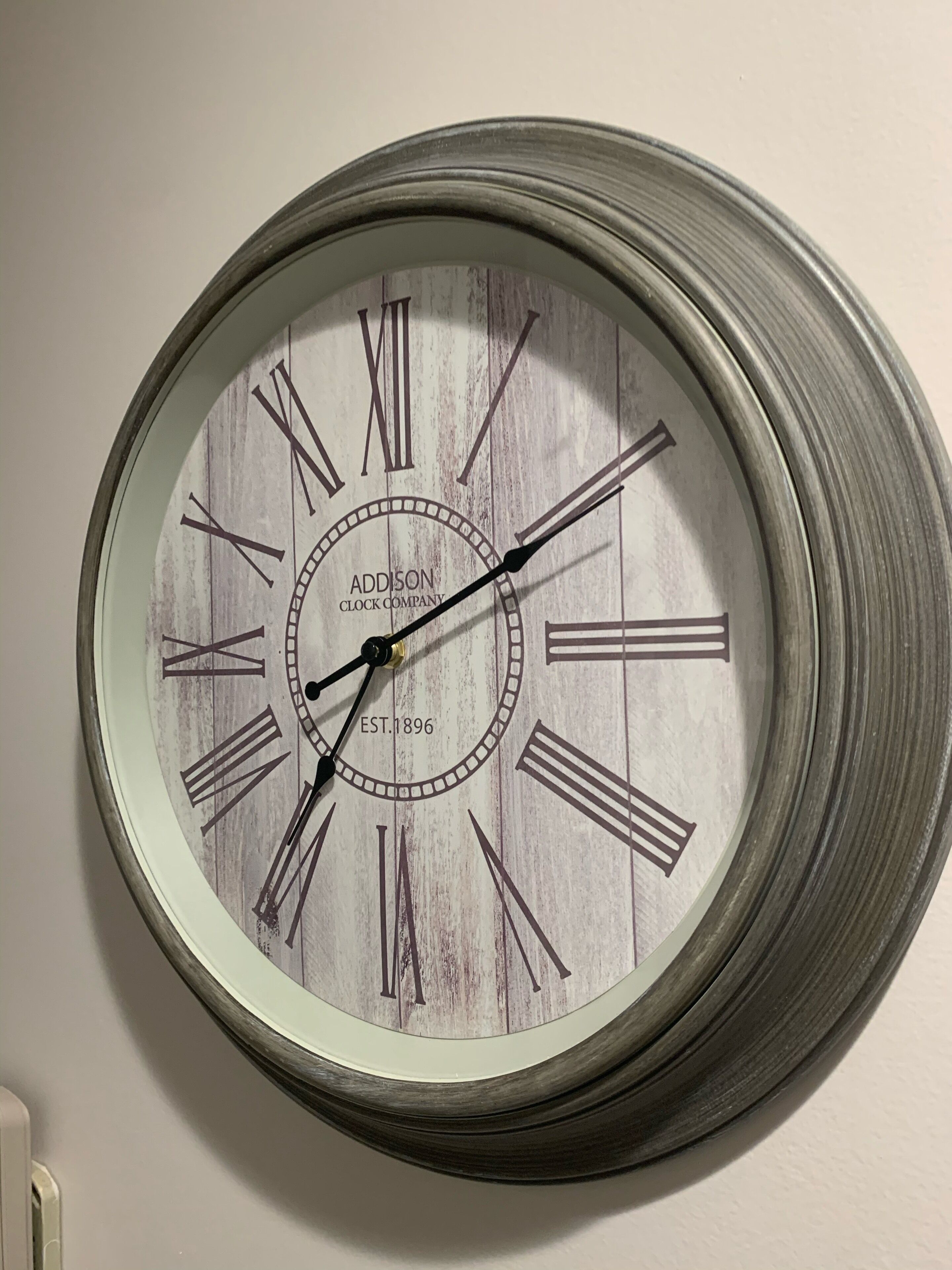 Um relógio de parede com números romanos e o nome da marca 'Addison Clock Company' e 'EST. 1896'.