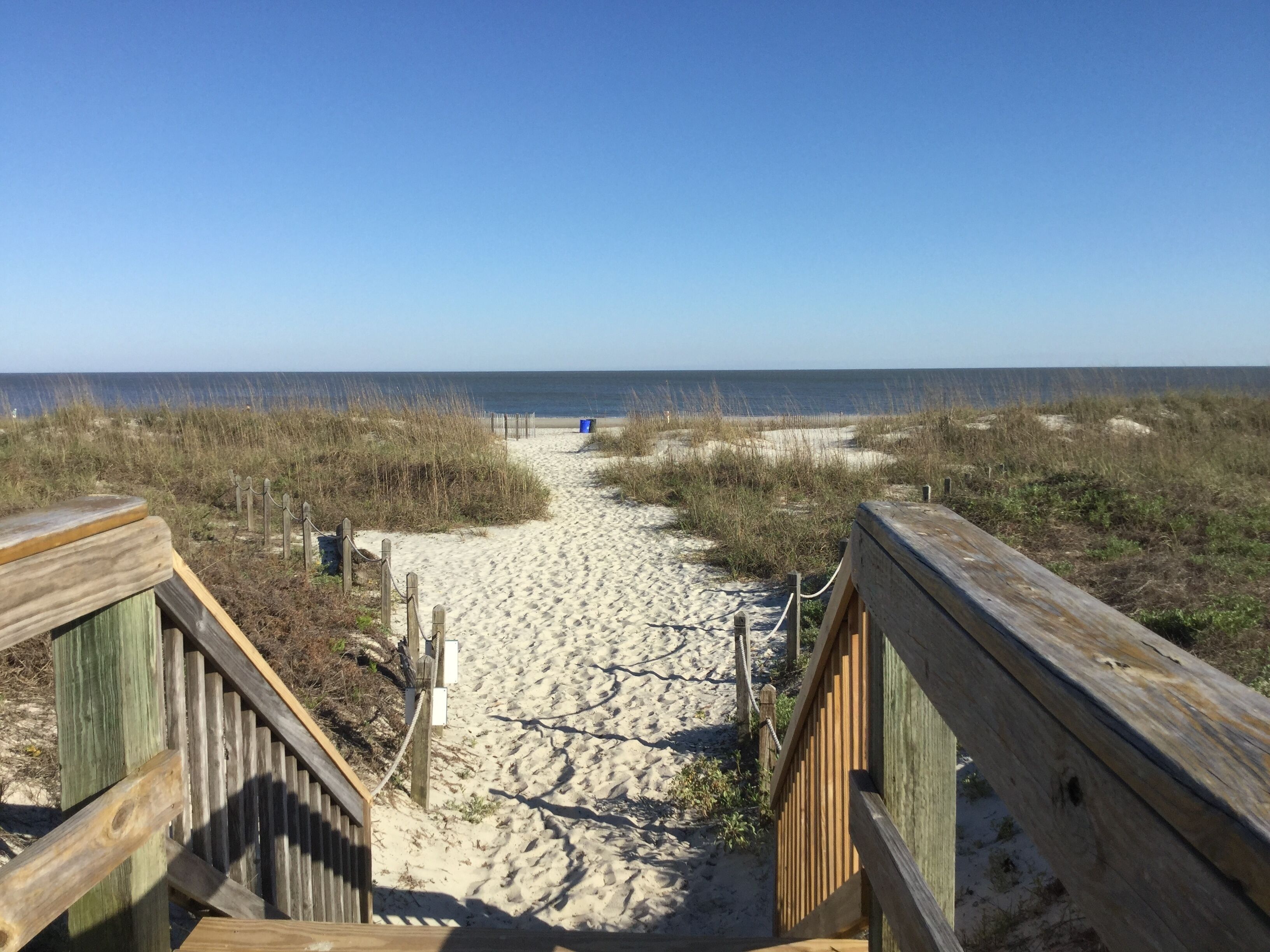 A sandy beach path leading to the ocean, flanked by wooden railings.