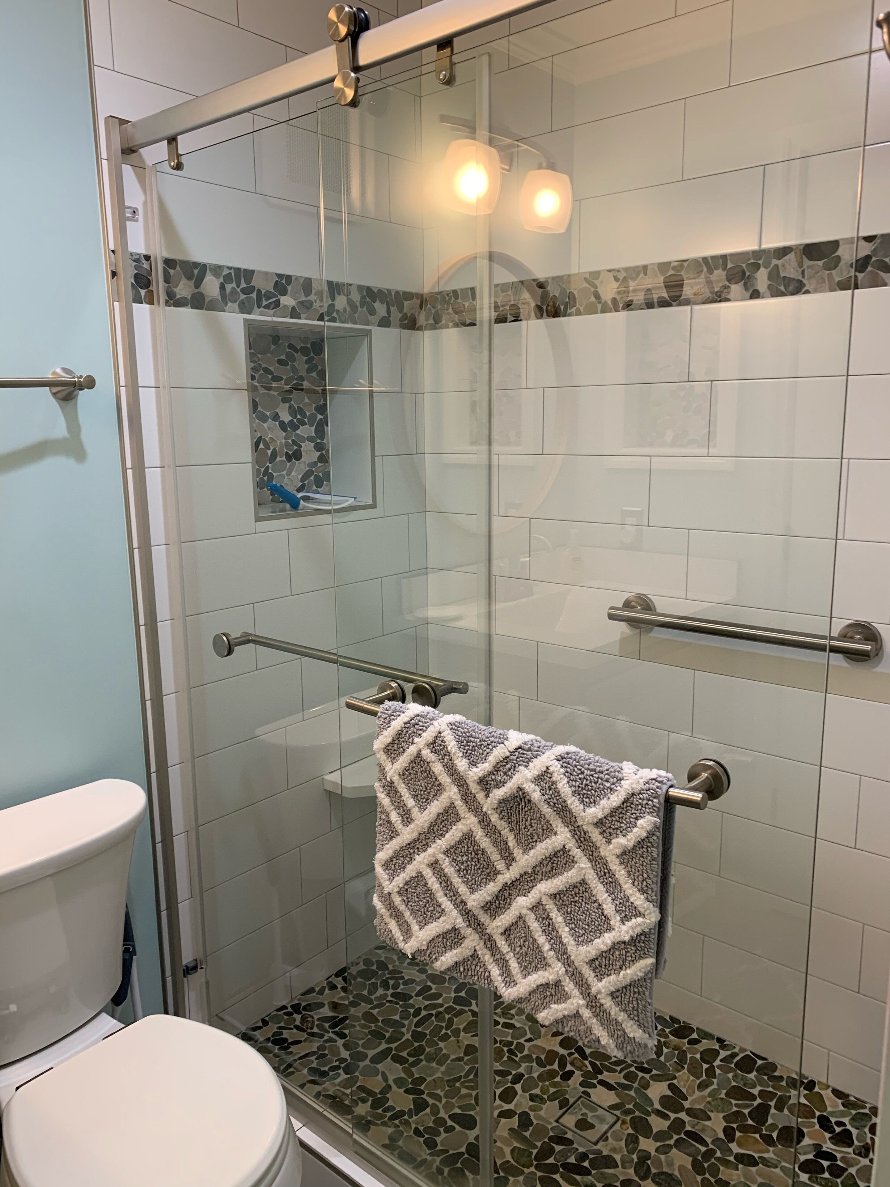 A glass-enclosed shower with a pebble-tiled floor and a towel rack.