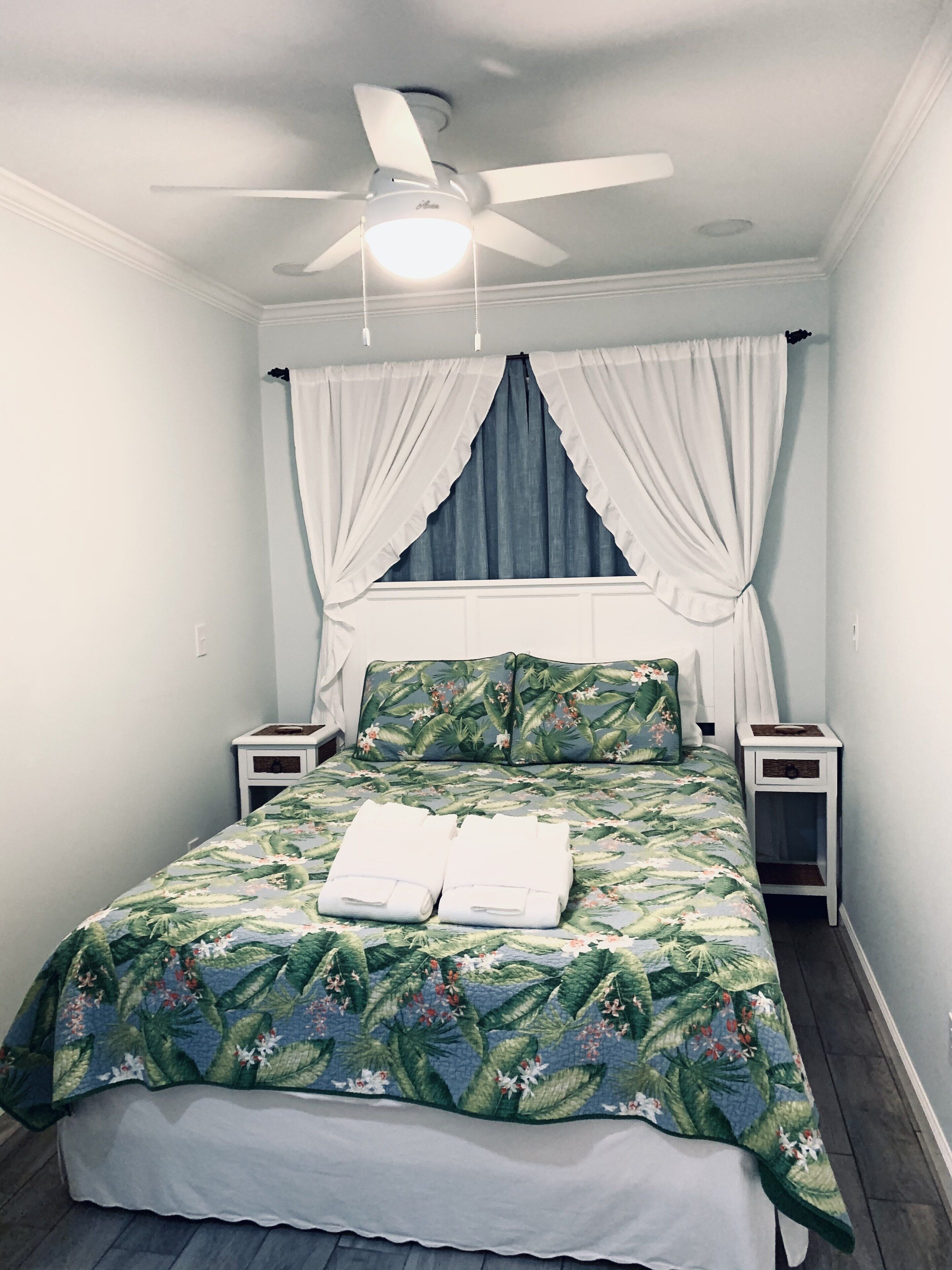 Ein Schlafzimmer mit einem Bett, einem Deckenventilator und einem Fenster mit Vorhängen.