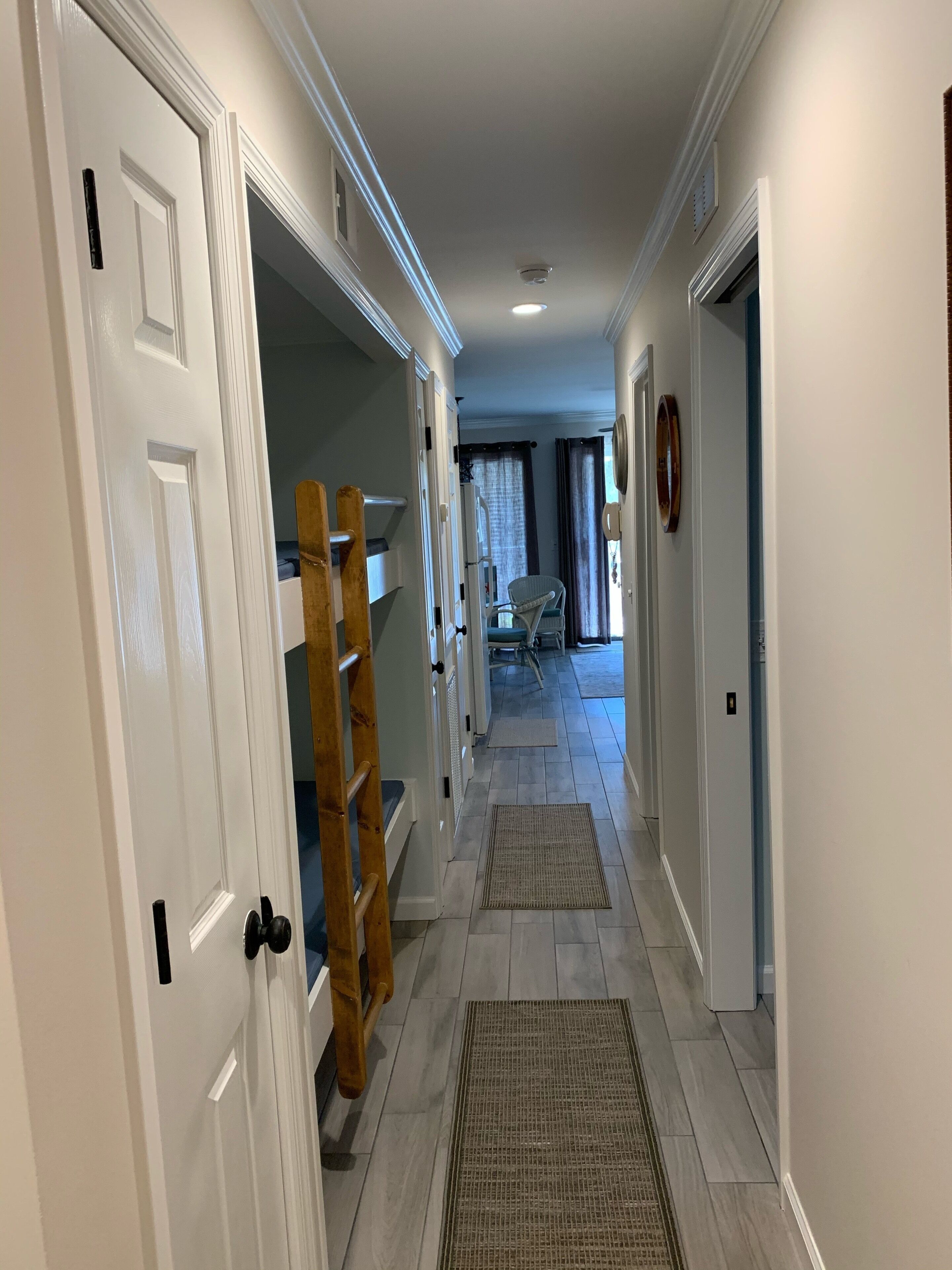 A narrow hallway with white doors, a wooden ladder, and a chair in the distance.