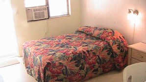 A small, simple room with a bed, a chair, and a desk.