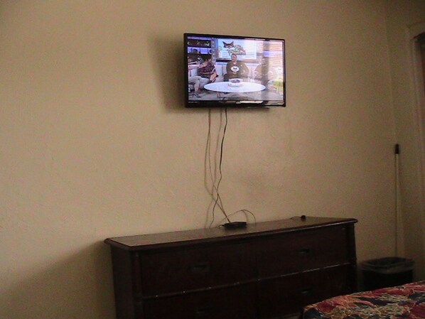 Un televisor montado en la pared sobre un aparador de madera oscura con un cubo de basura al lado.