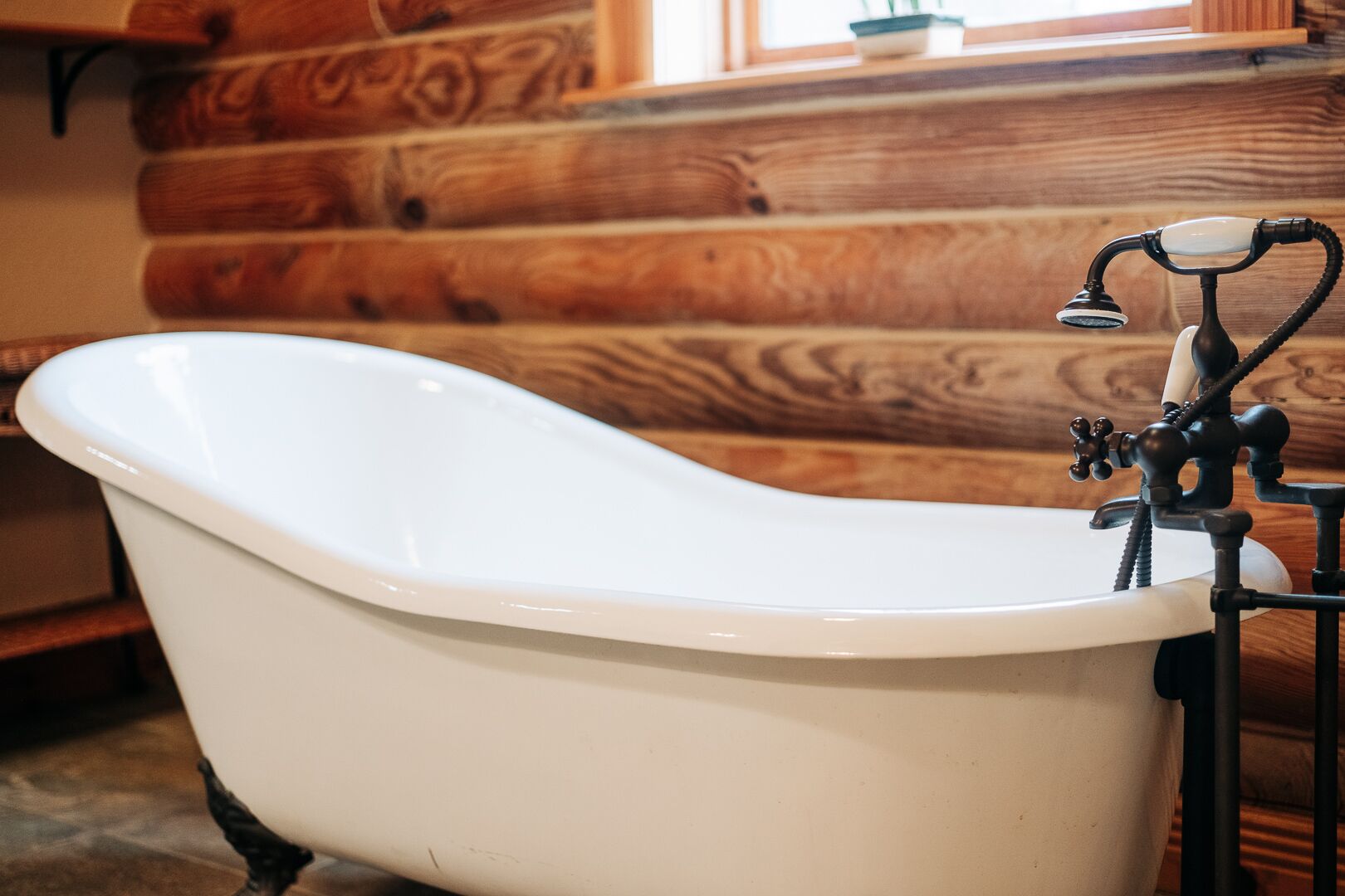 Een ligbad op poten in een rustieke kamer in chaletstijl, met houten wanden en een raam.