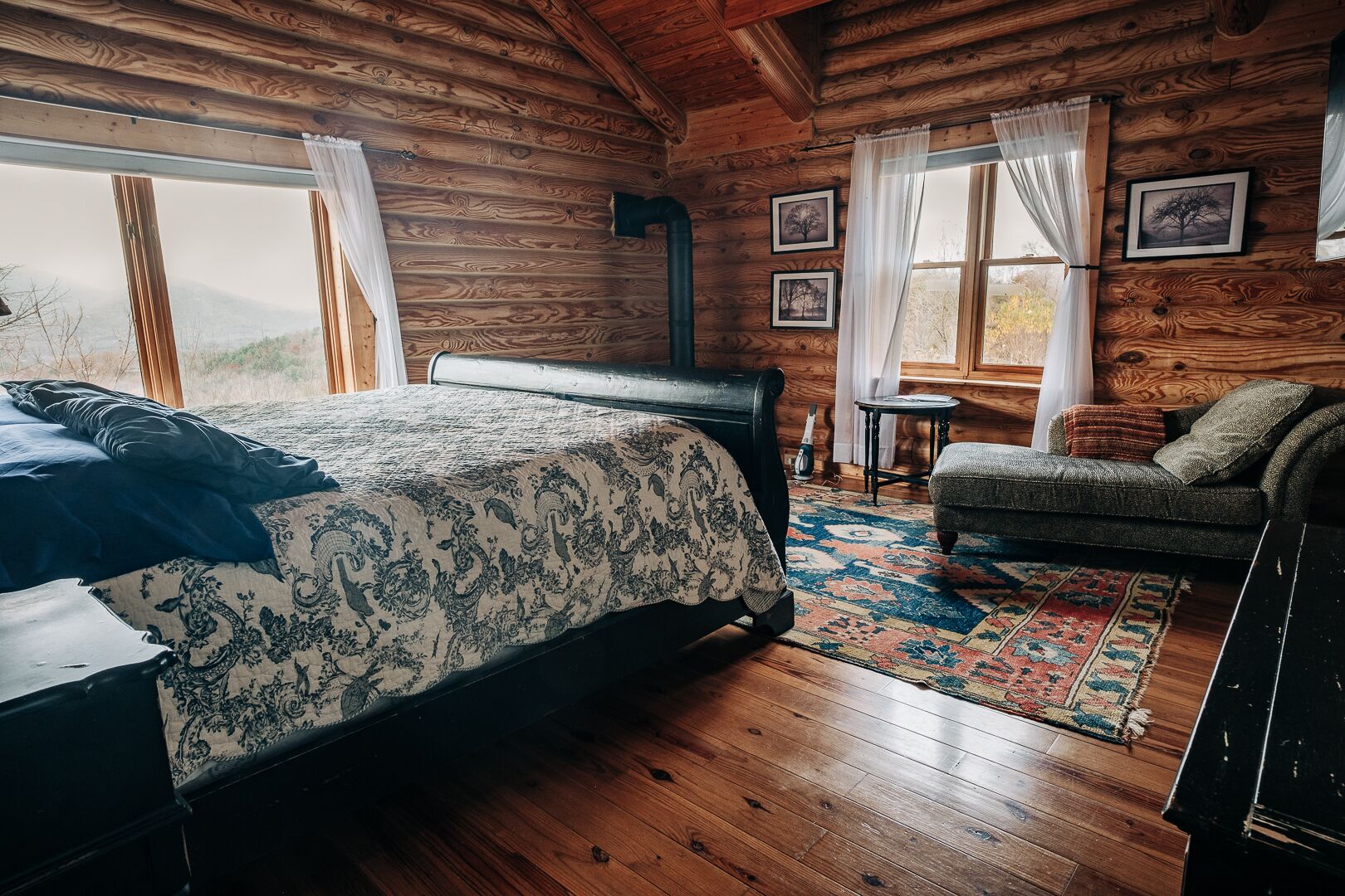 Ein Blockhauszimmer mit Bett, einer Couch, einem kleinen Tisch und einem Fenster mit Vorhängen.