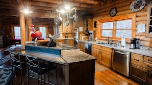 A rustic cabin-style kitchen with wooden walls, a central island with bar stools, stainless steel appliances, and a large window.