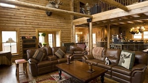 A log cabin interior with a living room featuring leather sofas, a coffee table, and a fireplace.