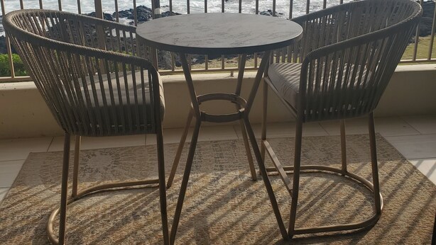 Ein Balkon mit Blick auf das Meer, mit zwei Korbstühlen und einem kleinen runden Tisch.