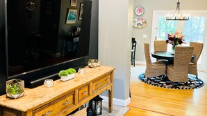 A modern living room with a flat-screen TV, wooden console table, and a dining area with wicker chairs and a chandelier. - NEWLY RENOVATED! 5-Star, Edgartown Colonial with Central AC (Edgartown)