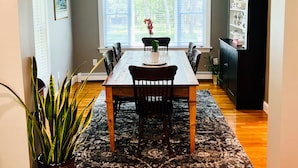 A dining area with a wooden table, chairs, a chandelier, and a potted plant. - NEWLY RENOVATED! 5-Star, Edgartown Colonial with Central AC (Edgartown)