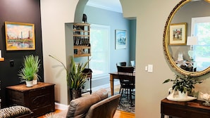 A living room with a sofa, coffee table, and a dining area with a table and chairs. There is a bookshelf, a mirror, and a potted plant. - NEWLY RENOVATED! 5-Star, Edgartown Colonial with Central AC (Edgartown)