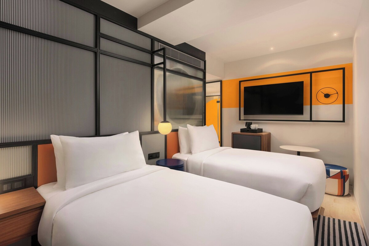 Una habitación de hotel con dos camas, un televisor, una mesita y un panel decorativo en la pared.