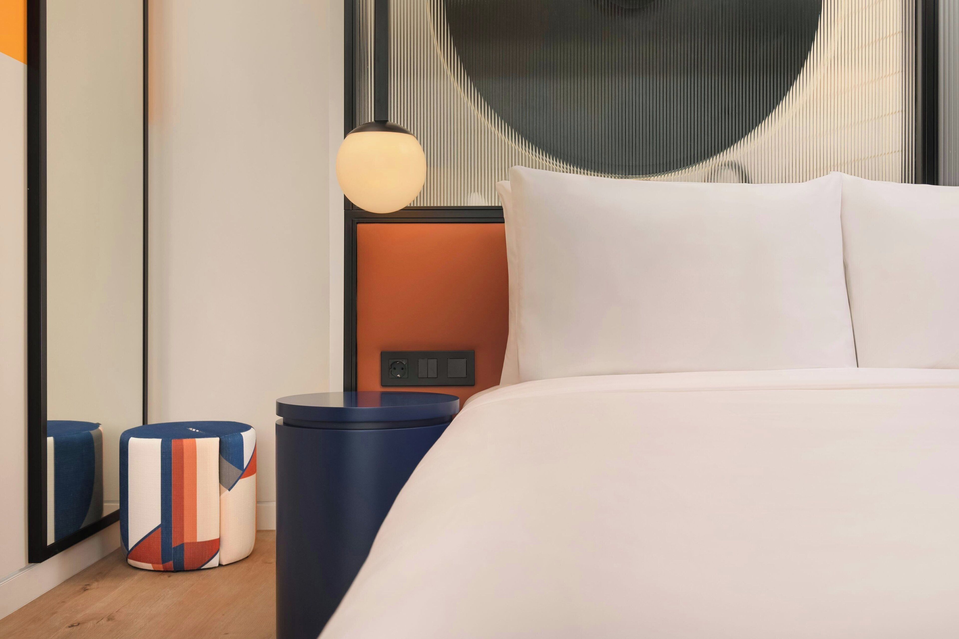 Ein modernes Hotelzimmer mit einem großen Bett, einem Nachttisch mit Lampe und einer Wand mit einem einzigartigen geometrischen Muster.