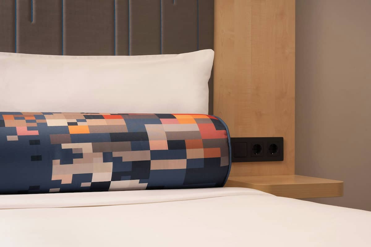 A bed with a white pillow and a colorful, pixelated blanket.