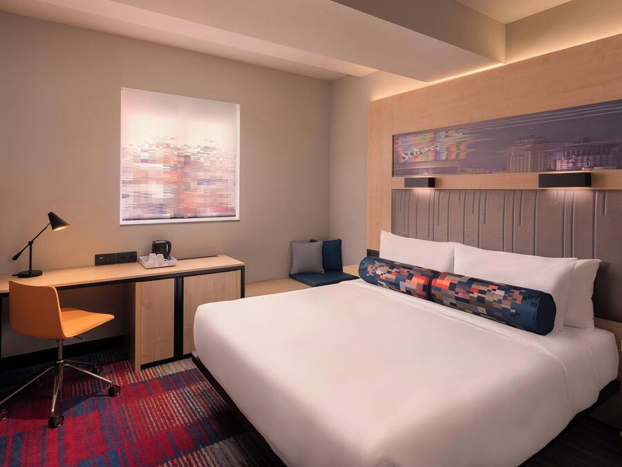 Habitación de hotel con cama, escritorio, silla y una obra de arte con vistas a la ciudad.