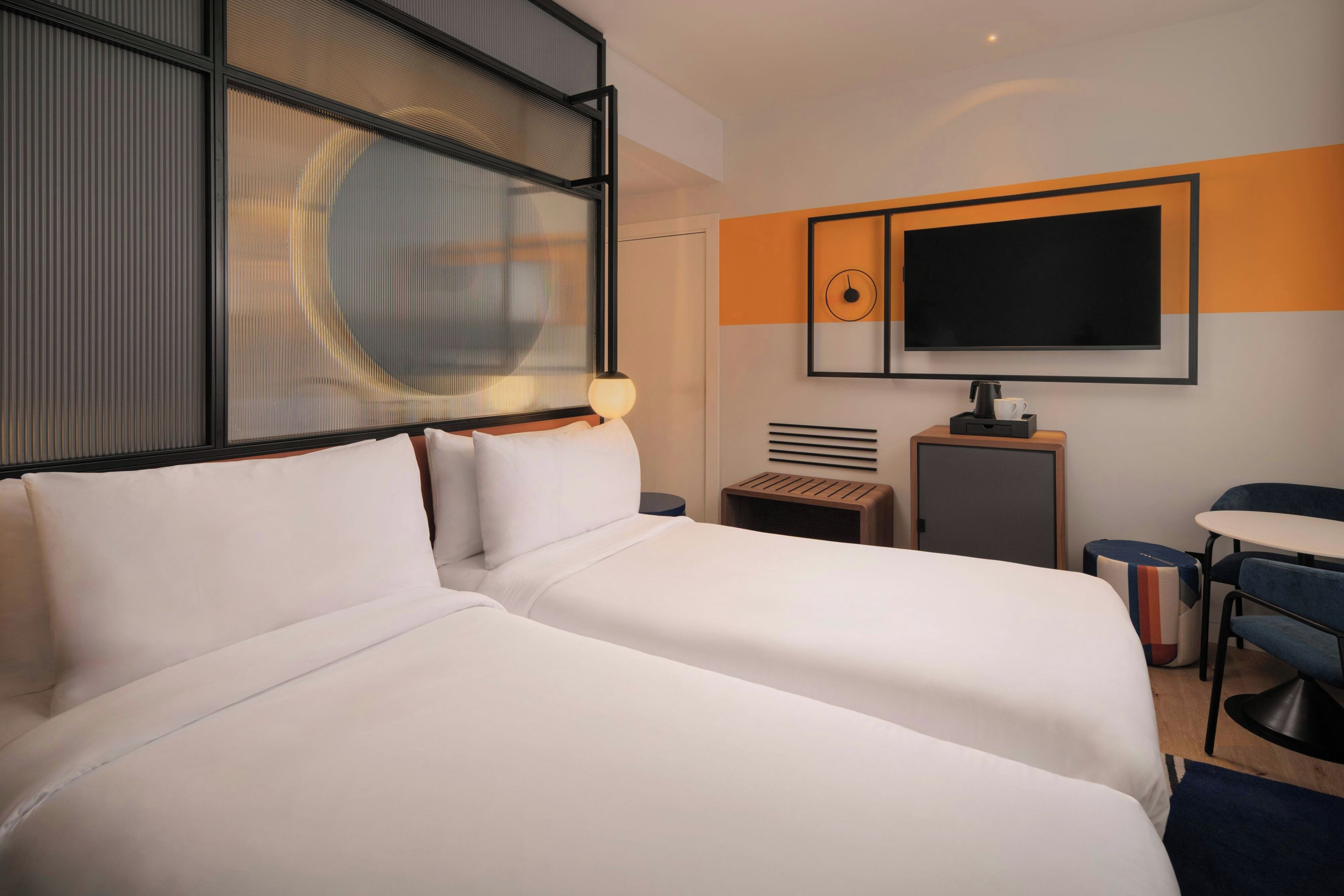 A hotel room with two beds, a TV, a coffee machine, and a small table.