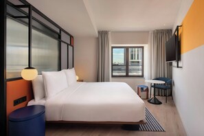 A modern hotel room with a large bed, a TV mounted on the wall, a small table with a chair, and a window with curtains. - Aloft by Marriott Madrid Gran Via (Madrid)