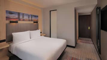 Habitación de hotel con una cama grande, una mesita de noche, un cuadro en la pared y una puerta que da a otra habitación.