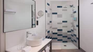 Un baño moderno con un espejo grande, un lavabo redondo y una ducha con pared de azulejos.