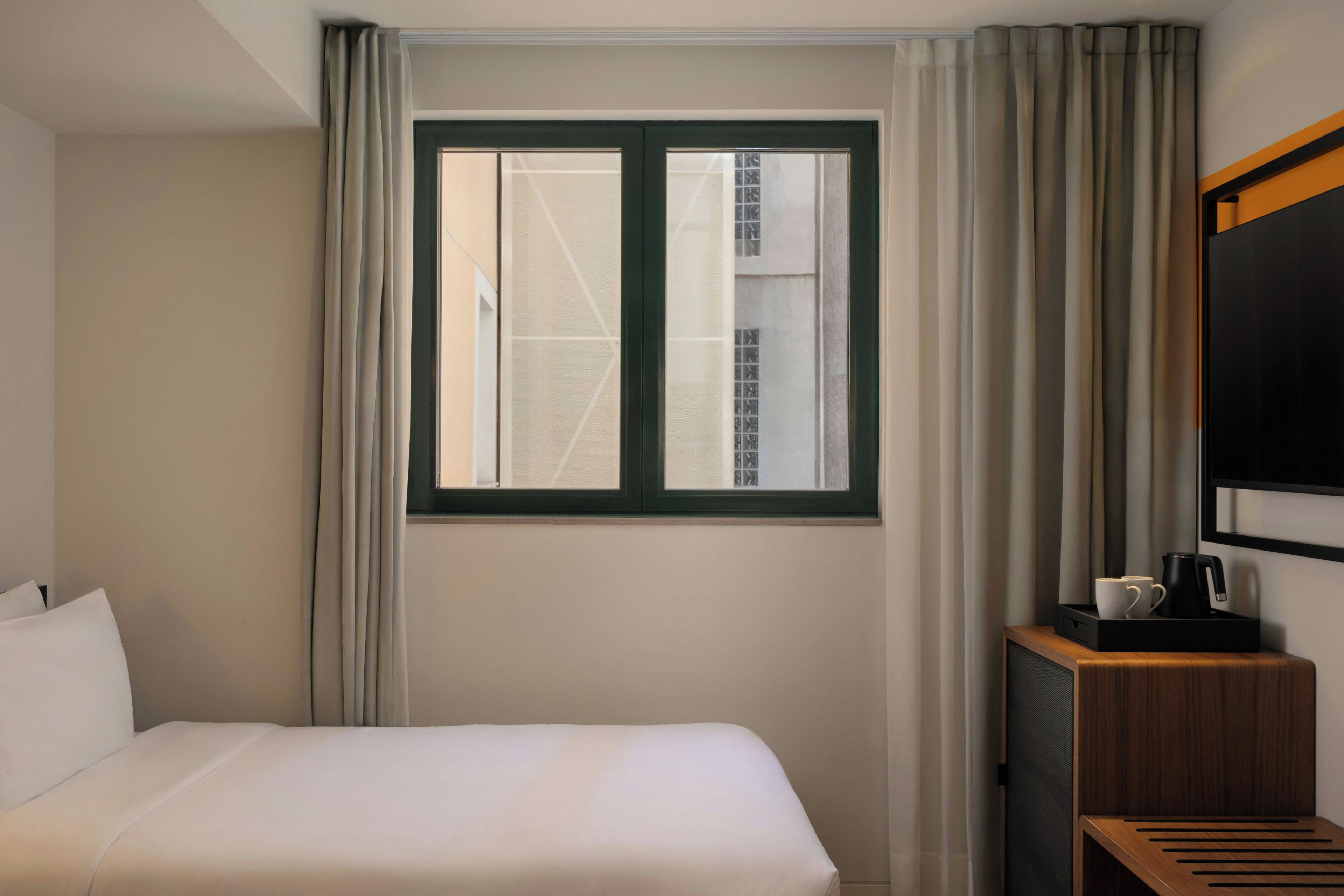 Ein Hotelzimmer mit einem Bett, einem Fenster mit Vorhängen, einem Flachbildfernseher und einem kleinen Tisch mit Wasserkocher und Tassen.