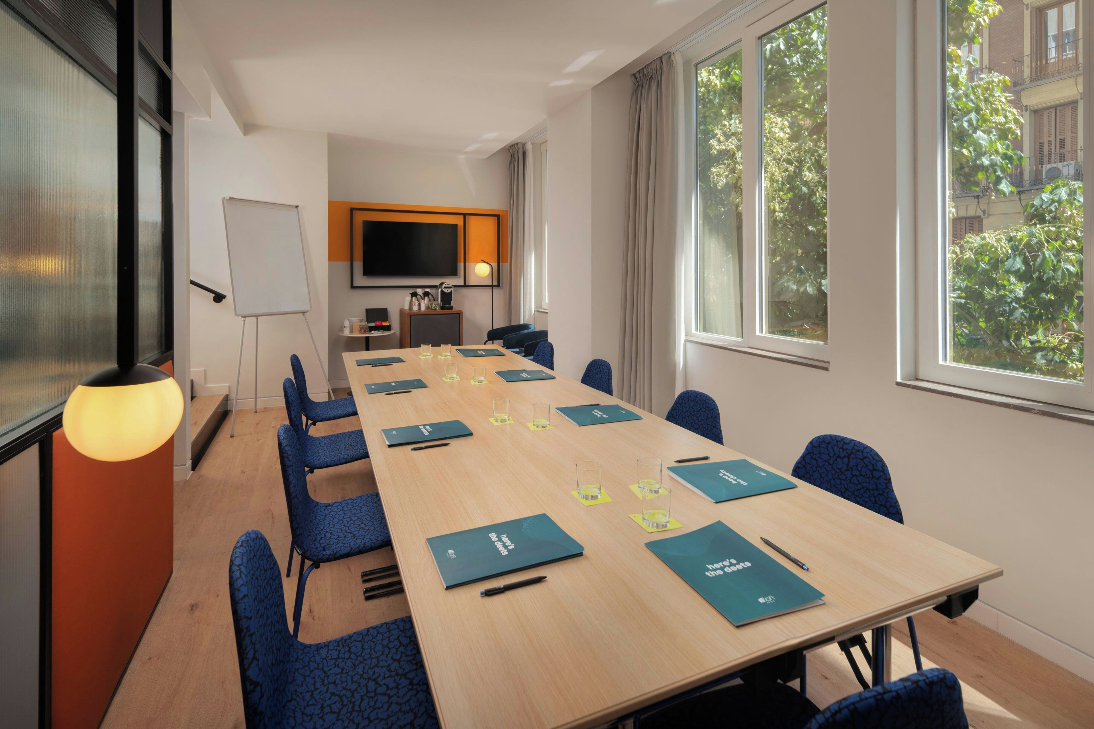 Una sala conferenze con un lungo tavolo, sedie, una lavagna e un televisore.