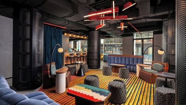 Een moderne lounge met een gestreept tapijt, zwart-wit gestreepte poefs en een blauwe bank.