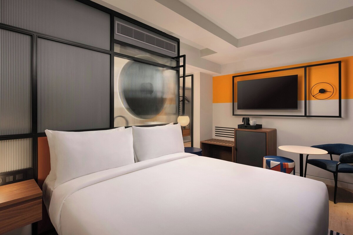 Una habitación de hotel moderna con una cama grande, un televisor de pantalla plana, un escritorio y una silla.