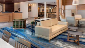 A modern hotel lobby with a reception desk, seating area, and a dining space.