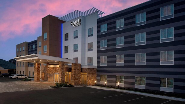 A Fairfield Inn by Marriott hotel with a modern design, featuring a prominent entrance and multiple floors.
