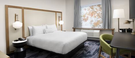 A hotel room with a large bed, bedside tables, a desk, a chair, and a window with curtains.