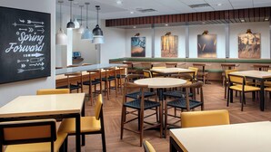 A restaurant with multiple tables and chairs, a blackboard with motivational writing, and artwork on the walls.