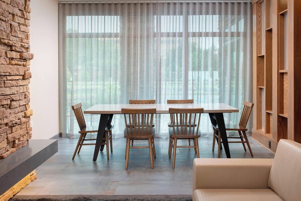 A modern dining area with a large table and four wooden chairs, a stone accent wall, and a large window with sheer curtains.