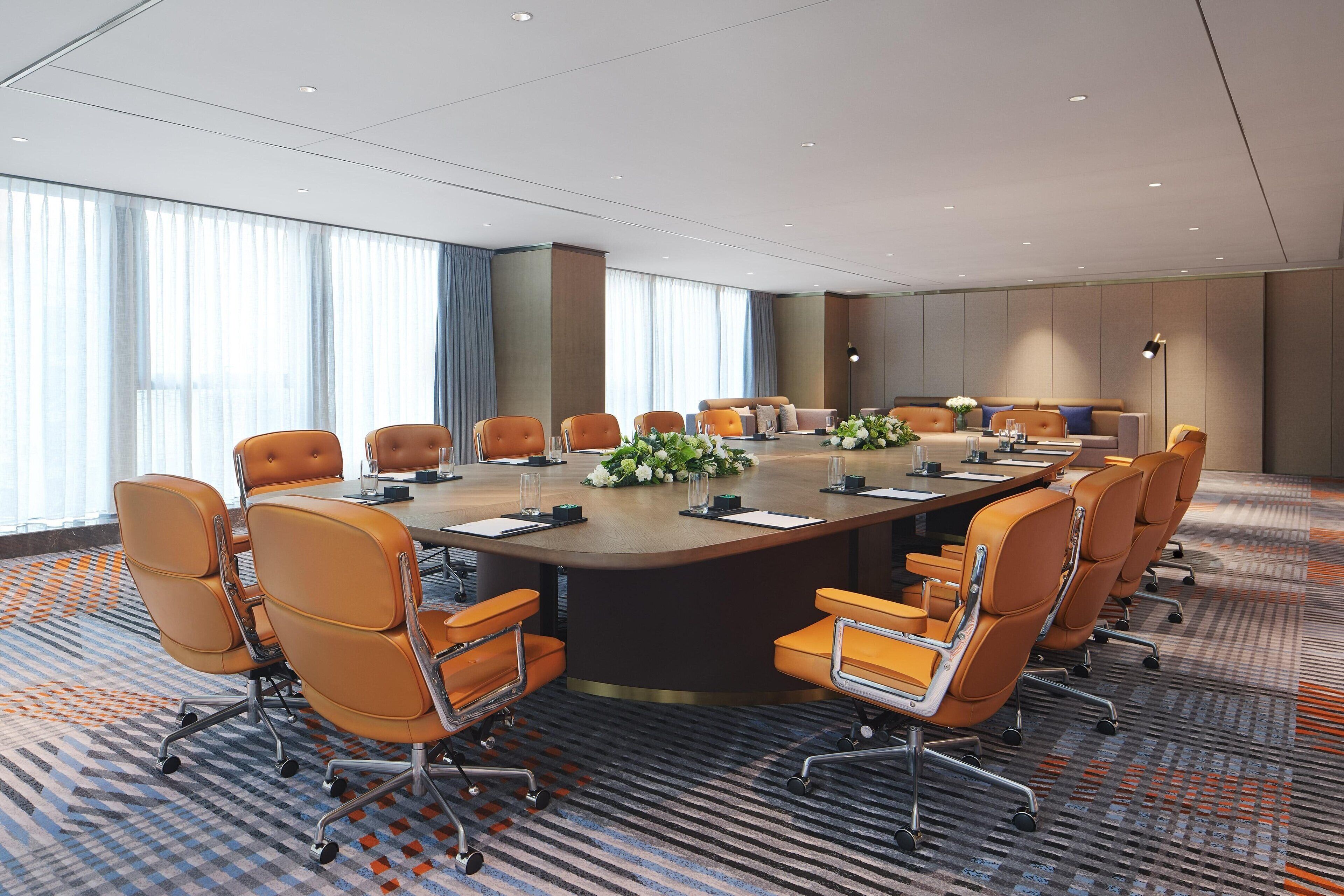 A conference room with a large oval table, multiple chairs, and a carpeted floor.