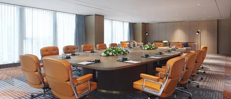 A conference room with a large oval table, multiple chairs, and a carpeted floor.