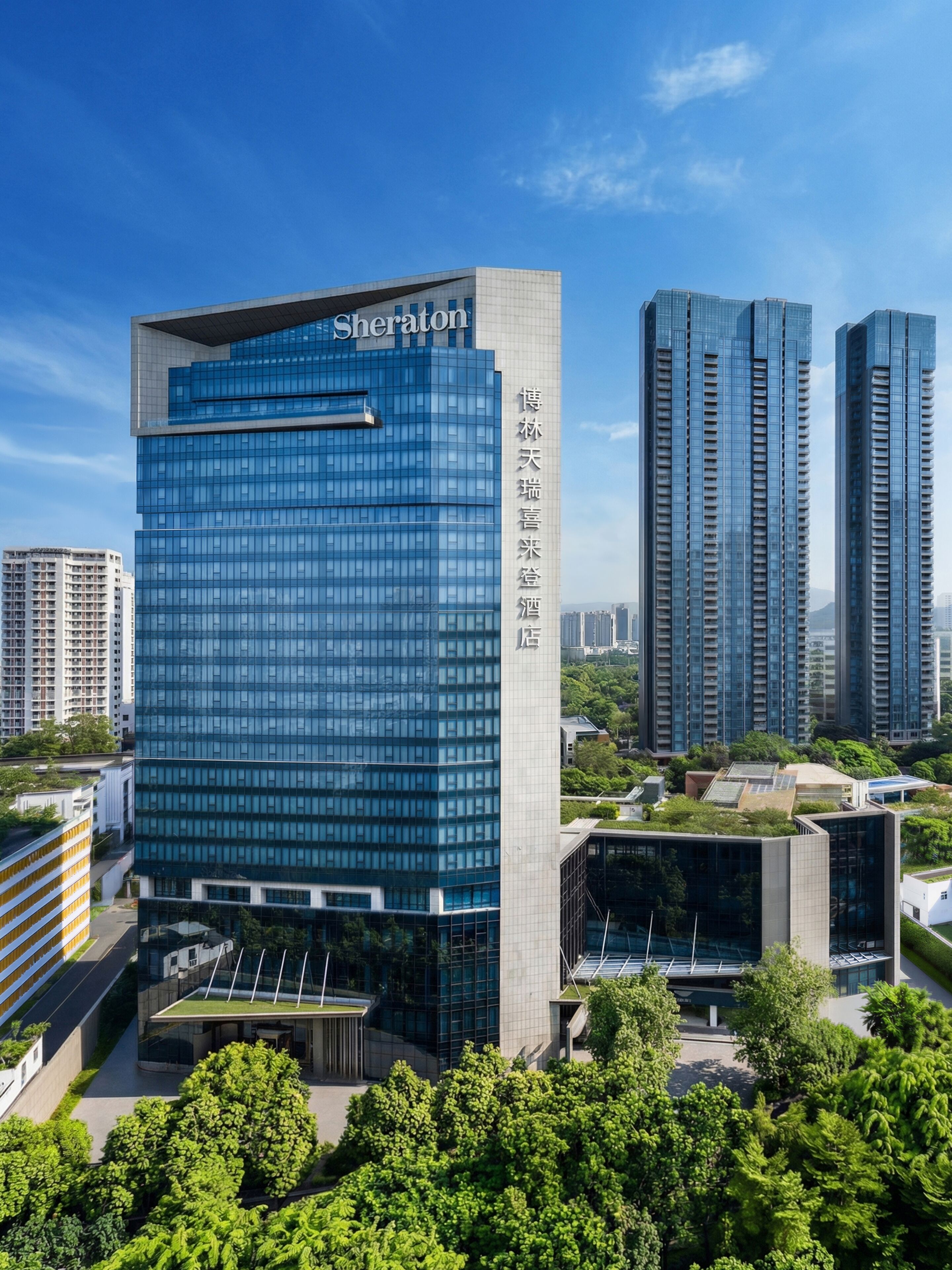 Un hôtel Sheraton doté d’une façade moderne en verre, entouré d’immeubles de grande hauteur et de verdure.