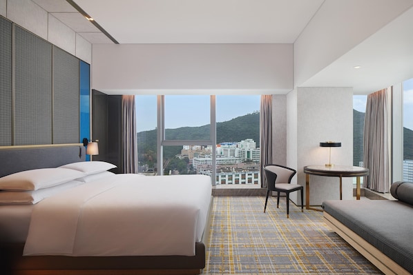 A hotel room with a large bed, a desk, a chair, and a sofa. The room has large windows with a city view. - Sheraton Shenzhen Nanshan (Shenzhen)