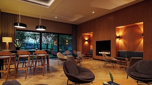 A modern hotel lobby with a fireplace, comfortable seating, and large windows offering a view of trees. - Four Points by Sheraton Warsaw Mokotow (Warsaw)