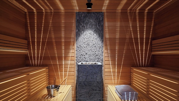 A sauna with wooden benches, a central stone wall, and a metal bucket. - Four Points by Sheraton Warsaw Mokotow (Warsaw)
