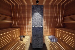 A sauna with wooden benches, a central stone wall, and a metal bucket. - Four Points by Sheraton Warsaw Mokotow (Warsaw)