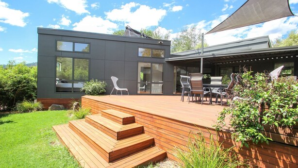 Una casa moderna con una terraza, un comedor con sillas y un ventanal grande.