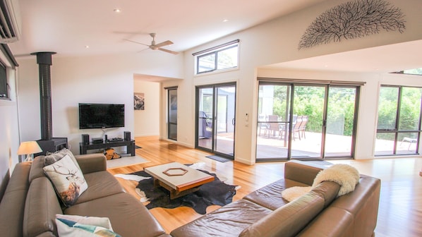 A spacious living room with a large flat-screen TV, leather sofas, a fireplace, and a sliding glass door leading to an outdoor patio.