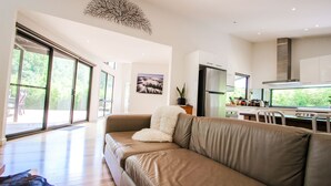 Una sala de estar moderna con un ventanal grande, un sofá y una cocina con refrigerador y estufa.