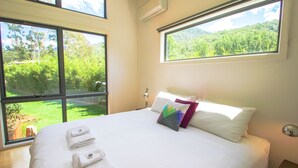 Un dormitorio con una cama grande, dos ventanas y vistas a zonas verdes.