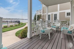 A covered porch with white wicker furniture and a view of a body of water.