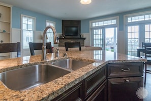A kitchen with granite countertops, a stainless steel sink, dark cabinetry, and a fireplace.