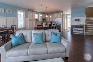 A living room with a sofa, a dining area with a table and chairs, a kitchen with appliances, and a staircase.