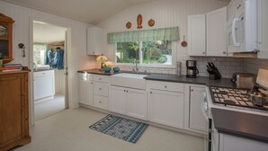 A kitchen with white cabinets, a stove, and a window with a view of greenery. - Summerland Stagecoach Cottage - A Historic Treasure in Summerland (Summerland)