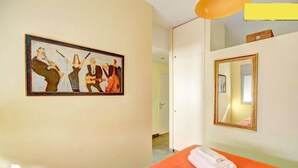 Une chambre d’hôtel avec un lit, un tableau au mur, un miroir et une porte donnant sur une autre pièce.