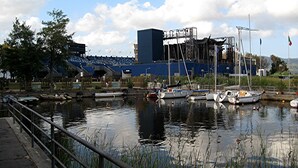 Un port de plaisance avec des bateaux amarrés, un grand bâtiment en arrière-plan et un ciel dégagé.